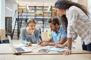 Group of three young multi-ethnic successful business people sitting in coworking space, talking
